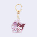 Die cut acrylic charm attached to gold ware keychain. Charm features an illustration of Kuromi sitting next to a purple jelly fruit dessert in a cup.