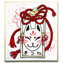 Illustration on board with gold outlining of a kitsune fox on a paper tag with a red rope with bells.