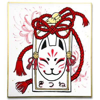 Illustration on board with gold outlining of a kitsune fox on a paper tag with a red rope with bells.