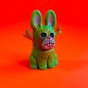 Vinyl figure of a green jackalope, sitting on the ground with blue hollowed eyes and antlers.