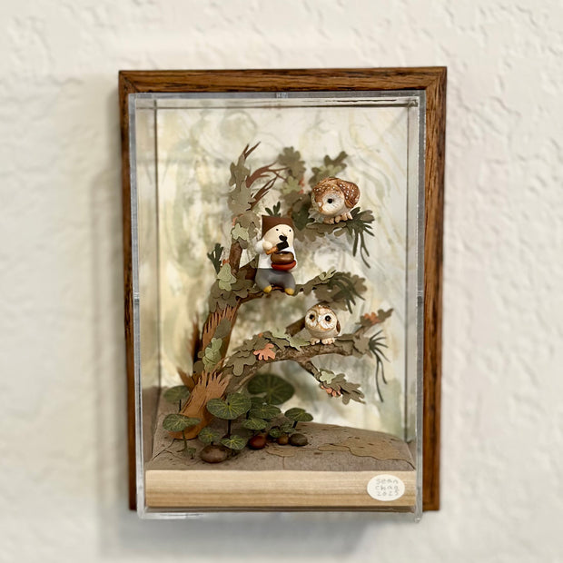 Mixed media sculpture of a person sitting on the branch of a tree, playing a sound bowl with small owls around them.