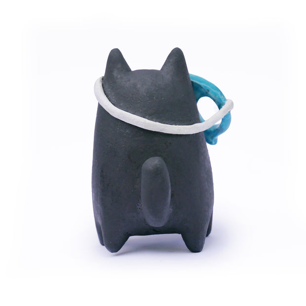Ceramic sculpture of a stylized black cat character, with a blue skull face mask that is slightly tilted off its face.