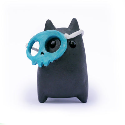 Ceramic sculpture of a stylized black cat character, with a blue skull face mask that is slightly tilted off its face.