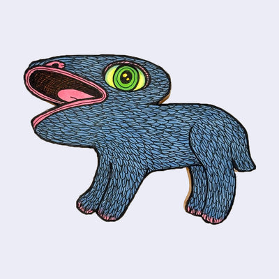 Illustration made with many lines, giving it the feel of a folk art woodcut on a die cut wood panel of a blue animal monster faced to the side with a large green eye and very large open mouth.