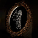 An ornate oval wall mirror with a carved, scrollwork bronze-brown frame, reflecting a black background with a white line-art illustration of a winged female figure.