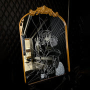 White engraved imagery on the surface of a mirror with gold gilding on the border. Imagery is of a woman looking over her shoulder with a shattered effect, splicing her face up.