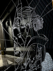 White engraved imagery on the surface of a mirror with gold gilding on the border. Imagery is of a woman looking over her shoulder with a shattered effect, splicing her face up.