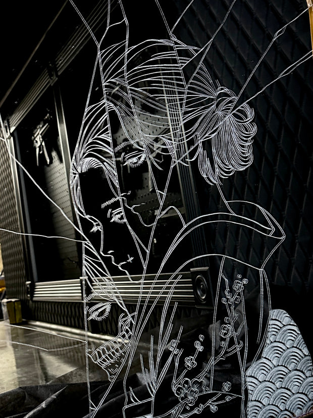 White engraved imagery on the surface of a mirror with gold gilding on the border. Imagery is of a woman looking over her shoulder with a shattered effect, splicing her face up.