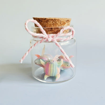 Set of 3 small sculptures shaped like flying chubby creatures. They have pastel stripes and are in a small glass bottle.