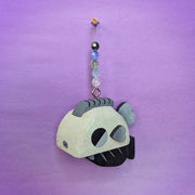 Wooden sculpture of a greyscale fish, with a bulky blocky body and tiny fins. It hangs from a chain wit beads on it.