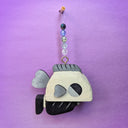 Wooden sculpture of a greyscale fish, with a bulky blocky body and tiny fins. It hangs from a chain wit beads on it.