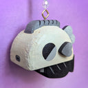 Wooden sculpture of a greyscale fish, with a bulky blocky body and tiny fins. It hangs from a chain wit beads on it.