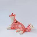 Ceramic figurine of a white and pink fox with 3 tails and patterned fur. It has red "wind" designs on it and gold painted accents.