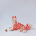 Ceramic figurine of a white and pink fox with 3 tails and patterned fur. It has red "wind" designs on it and gold painted accents.