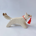 White ceramic sculpture of a dog like creature with a tassel hanging from its mouth and 2 tails. It has a necklace made of fangs as its collar.