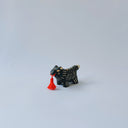 Small black ceramic sculpture of a wolf-like animal with a red tassel hanging from its mouth.