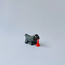 Small black ceramic sculpture of a wolf-like animal with a red tassel hanging from its mouth.