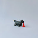 Small black ceramic sculpture of a wolf-like animal with a red tassel hanging from its mouth.
