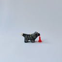 Small black ceramic sculpture of a wolf-like animal with a red tassel hanging from its mouth.