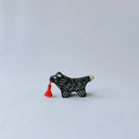 Small black ceramic sculpture of a wolf-like animal with a red tassel hanging from its mouth.