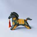 Black matte ceramic figure of a horse with carved decorative elements of orange poppy flowers, orange flames and an orange blanket. It has an orange tassel in its mouth.