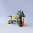 Black matte ceramic figure of a horse with carved decorative elements of orange poppy flowers, orange flames and an orange blanket. It has an orange tassel in its mouth.