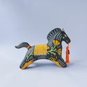 Black matte ceramic figure of a horse with carved decorative elements of orange poppy flowers, orange flames and an orange blanket. It has an orange tassel in its mouth.
