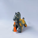 Black matte ceramic figure of a horse with carved decorative elements of orange poppy flowers, orange flames and an orange blanket. It has an orange tassel in its mouth.