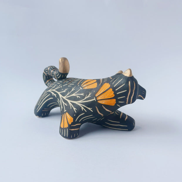 Black sgraffito ceramic sculpture of a tiger, with a long body and a carved pattern of orange poppy flowers.