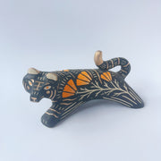 Black sgraffito ceramic sculpture of a tiger, with a long body and a carved pattern of orange poppy flowers.