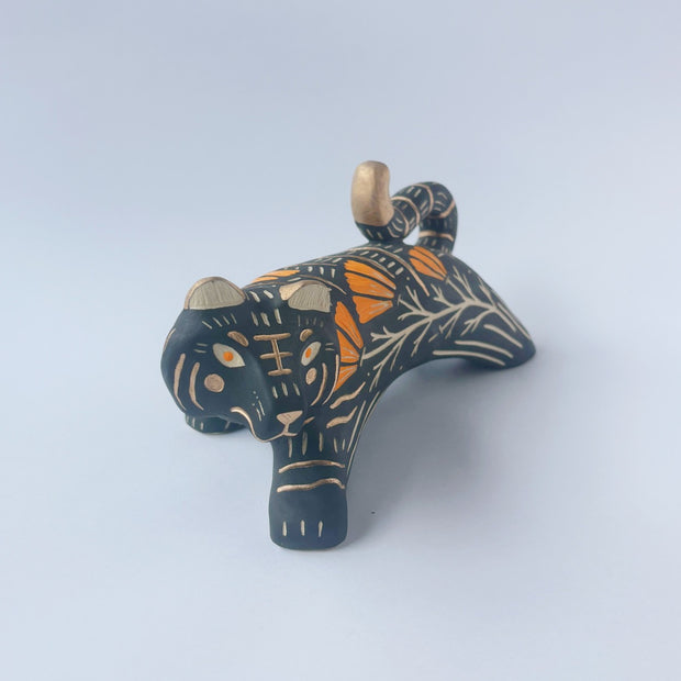 Black sgraffito ceramic sculpture of a tiger, with a long body and a carved pattern of orange poppy flowers.