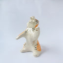 Glossy ceramic sculpture of a white and orange tiger, leaning back on its hindlegs with its front legs up and its head thrown back.