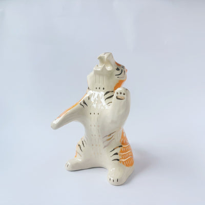 Glossy ceramic sculpture of a white and orange tiger, leaning back on its hindlegs with its front legs up and its head thrown back.