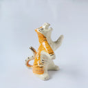Glossy ceramic sculpture of a white and orange tiger, leaning back on its hindlegs with its front legs up and its head thrown back. It has an orange poppy flower pattern on its back.