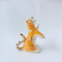 Glossy ceramic sculpture of a white and orange tiger, leaning back on its hindlegs with its front legs up and its head thrown back. It has an orange poppy flower pattern on its back.