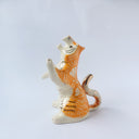 Glossy ceramic sculpture of a white and orange tiger, leaning back on its hindlegs with its front legs up and its head thrown back. It has an orange poppy flower pattern on its back.