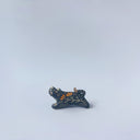 Very small black sgraffito ceramic sculpture of a tiger, with a long body and a carved pattern of orange poppy flowers.