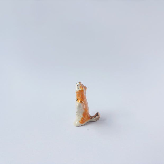 Very small ceramic sculpture of a white and orange tiger, leaning back on its hindlegs with its front legs up and its head thrown back.