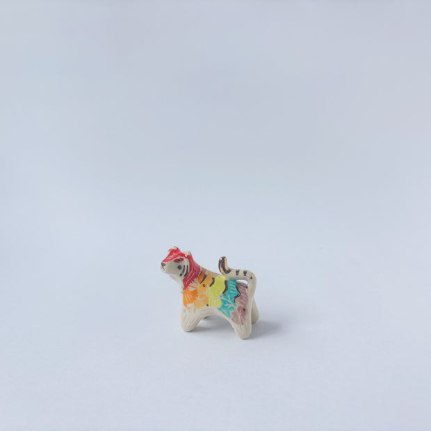 Very small ceramic sculpture of a tiger with a white underbelly and rainbow coloring on its back with gold detailing.