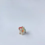 Very small ceramic sculpture of a tiger with a white underbelly and rainbow coloring on its back with gold detailing.