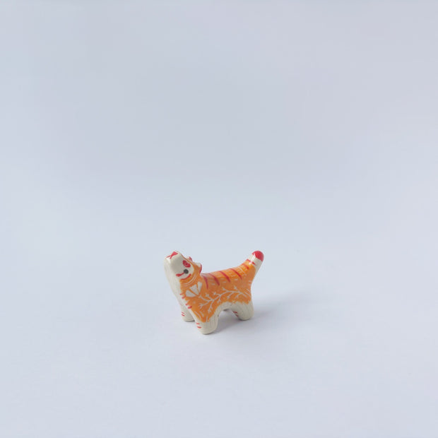 Very small ceramic sculpture of a tiger with a white underbelly and orange fur with red stripes, gold detailing and white carved poppy flowers. It is in a roaring stance.