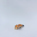 Very small glossy ceramic sculpture of a tiger, laying down asleep. It has a carved poppy flower pattern and gold detailing.