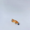Very small glossy ceramic sculpture of a tiger, laying down asleep. It has a carved poppy flower pattern and gold detailing.