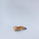Very small glossy ceramic sculpture of a tiger, laying down asleep. It has a carved poppy flower pattern and gold detailing.