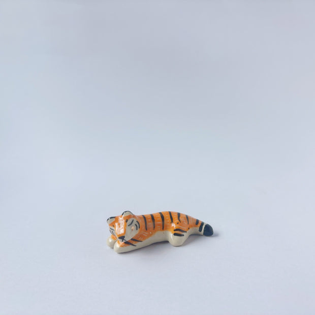 Very small glossy ceramic sculpture of a tiger, laying down asleep. It has a carved poppy flower pattern and gold detailing.