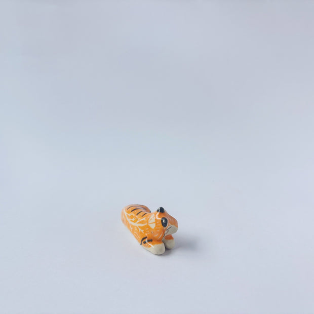 Very small glossy ceramic sculpture of a tiger, laying down asleep. It has a carved poppy flower pattern and gold detailing.