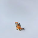 Very small glossy ceramic sculpture of a lion, sitting with a magpie on its back. The tiger has a carved poppy flower design on its back and gold detailing.