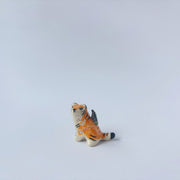 Very small glossy ceramic sculpture of a lion, sitting with a magpie on its back. The tiger has a carved poppy flower design on its back and gold detailing.