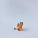 Very small glossy ceramic sculpture of a lion, sitting with a magpie on its back. The tiger has a carved poppy flower design on its back and gold detailing.