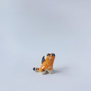 Very small glossy ceramic sculpture of a lion, sitting with a magpie on its back. The tiger has a carved poppy flower design on its back and gold detailing.